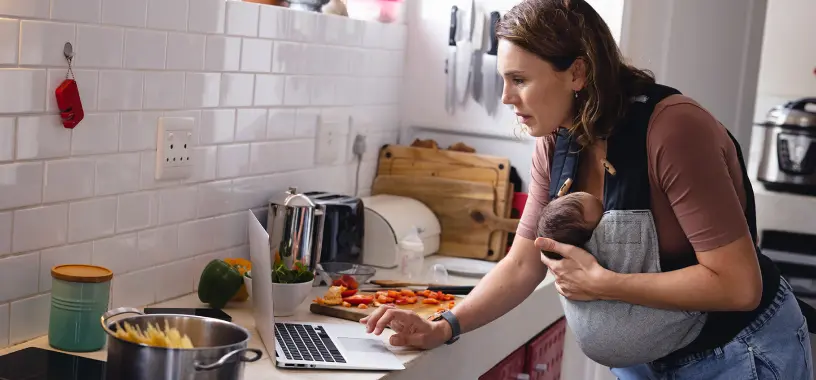 A busy specialty pharmacy patient holding her infant child while looking at her laptop screen
