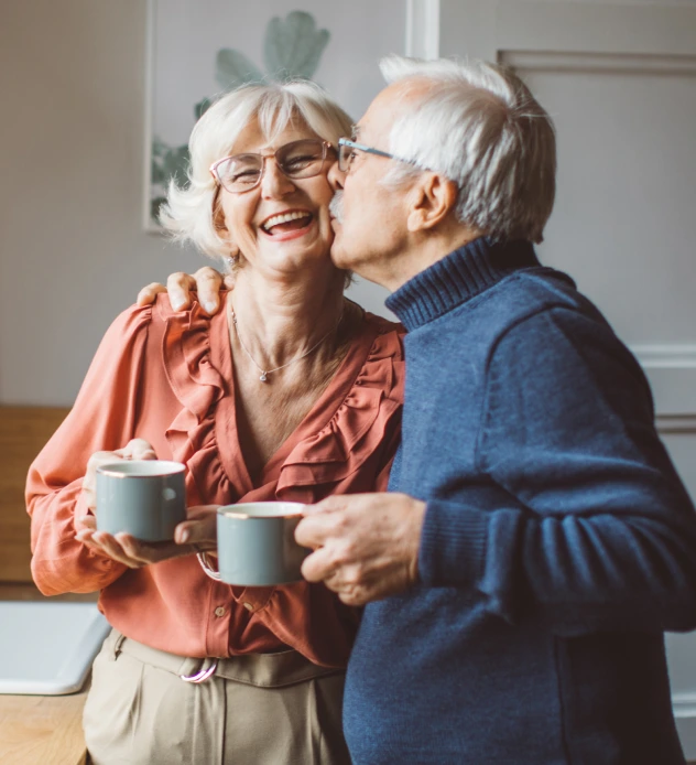 A specialty pharmacy patient kissing his wife on the cheek as she smiles and laughs