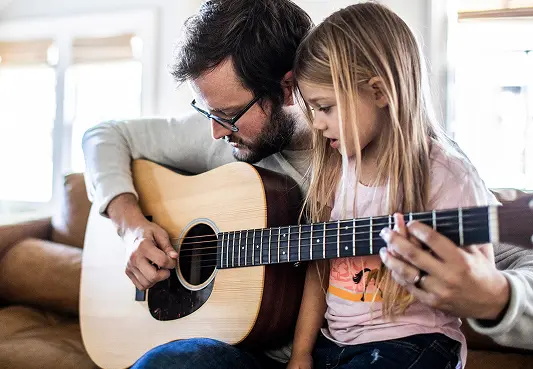 A specialty pharmacy patient showing his daughter how to strum a chord on a guitar