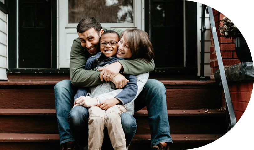 A specialty pharmacy patient embracing his wife and their 10-year-old son on the front steps of their home