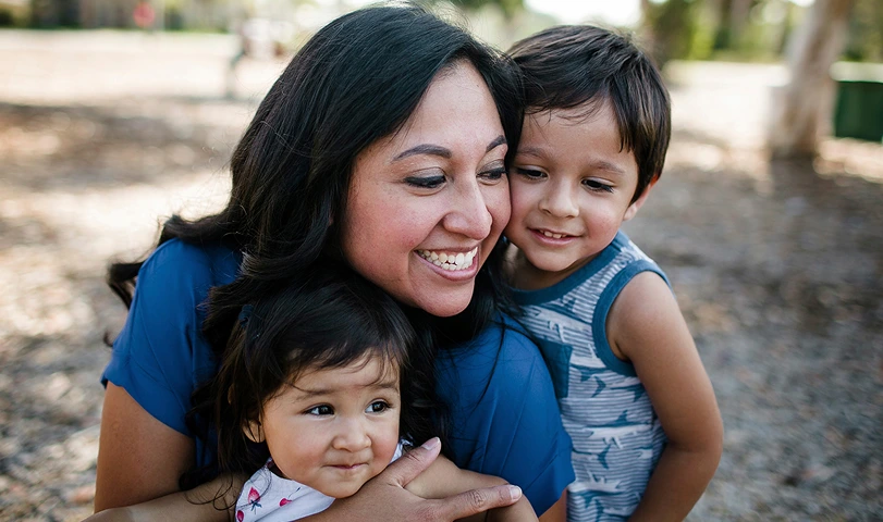 A pediatric specialty pharmacy patient is embraced by her mother and older brother